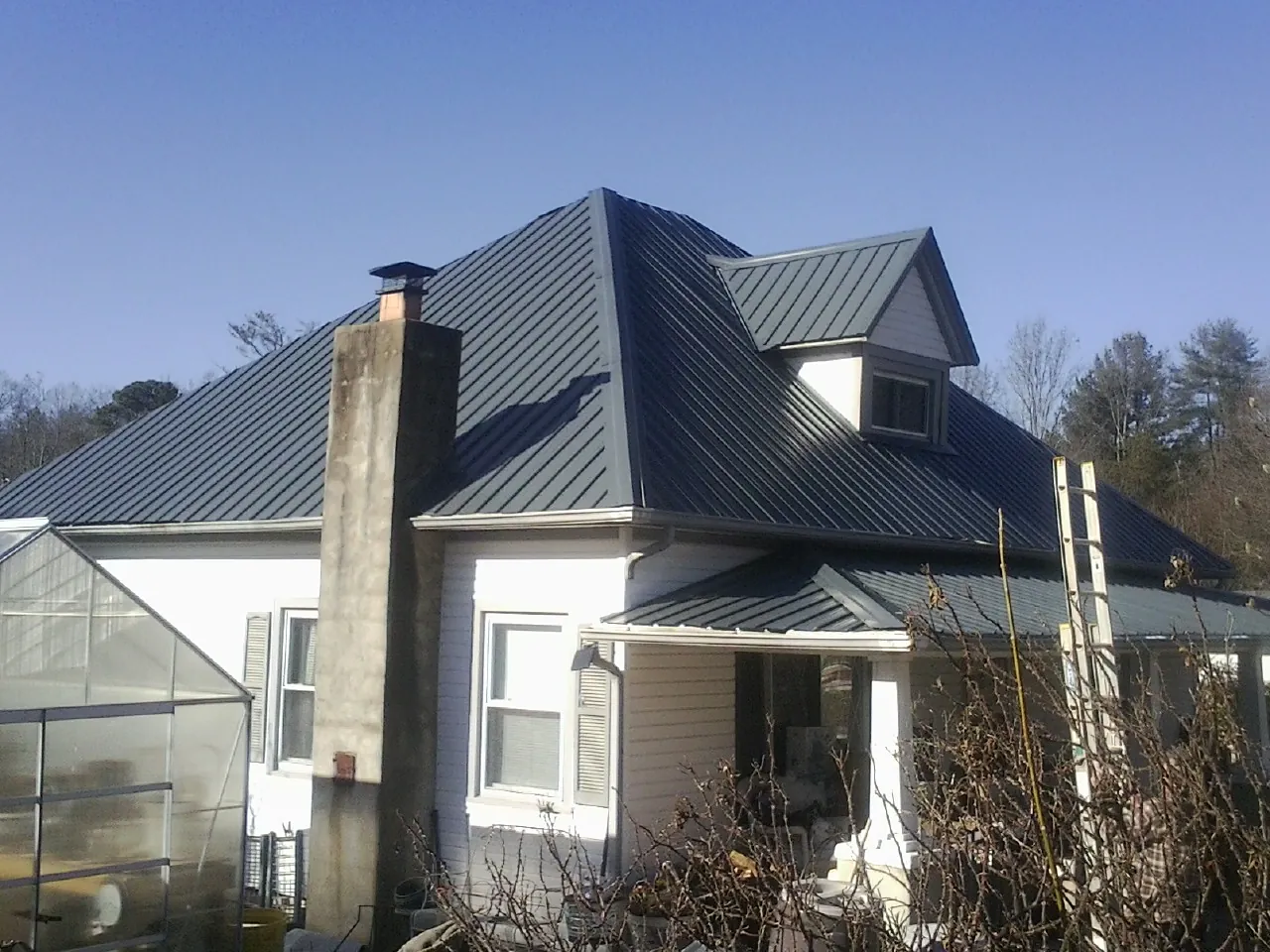 Dark blue standing seam metal roof on a white farmhouse with dormer — Slate & Tile Roof Repair by Roofing Brothers in Medora