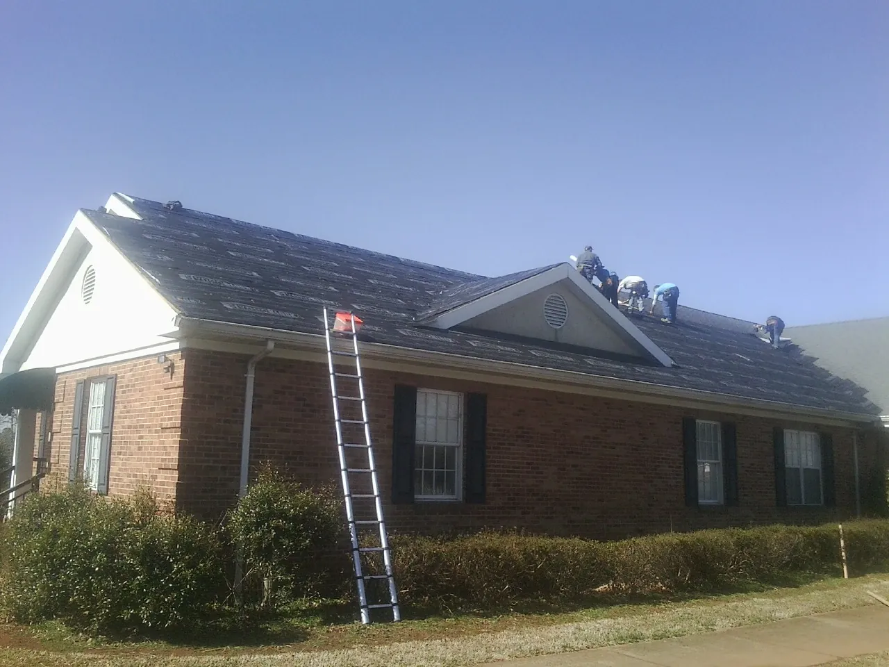 Crew tearing shingles off a brick ranch roof with a ladder set — Metal Roof Repair work by our crew in Medora