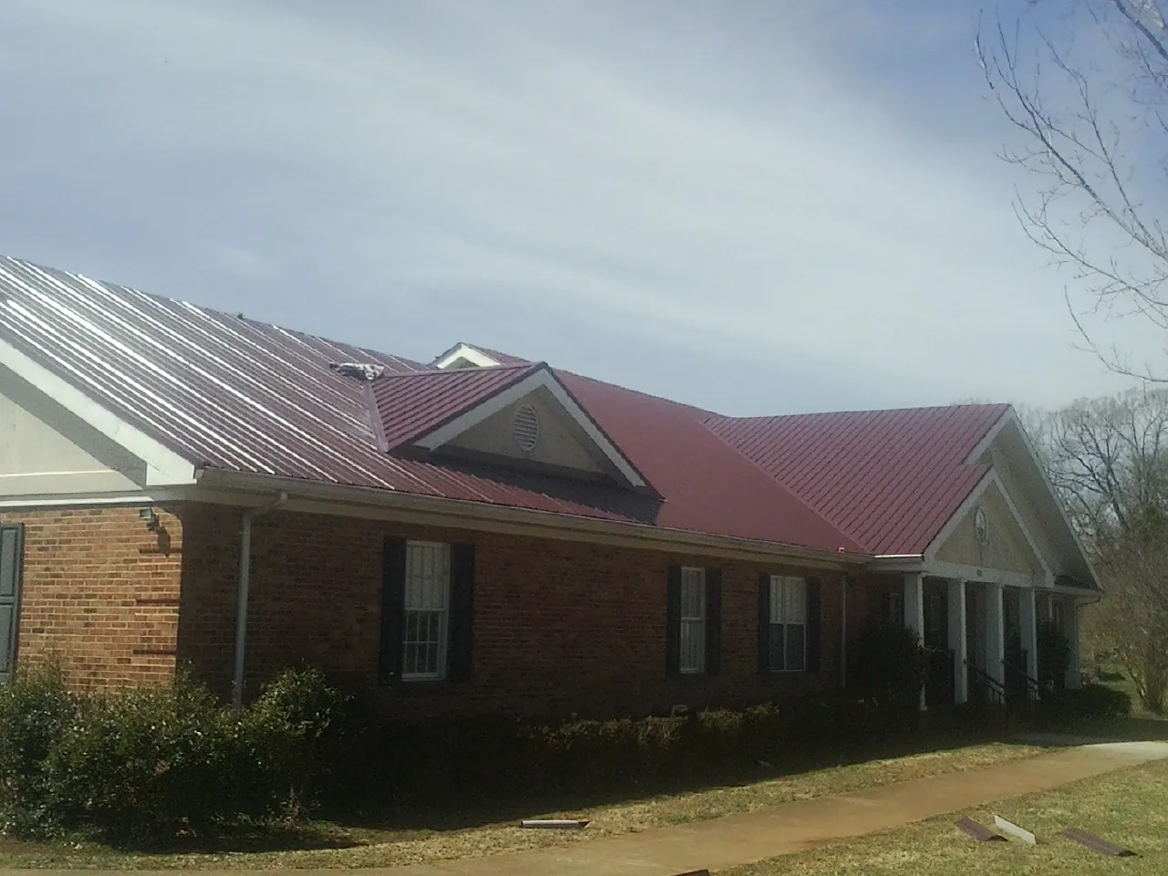 Red metal roof with gabled entries on a long brick building, from a Hail Damage Roof Repair job in Medora