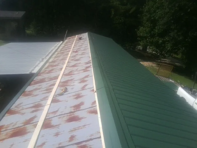 Old rusted panels beside newly installed green metal roofing — Wind Damage Roof Repair by Roofing Brothers in Medora