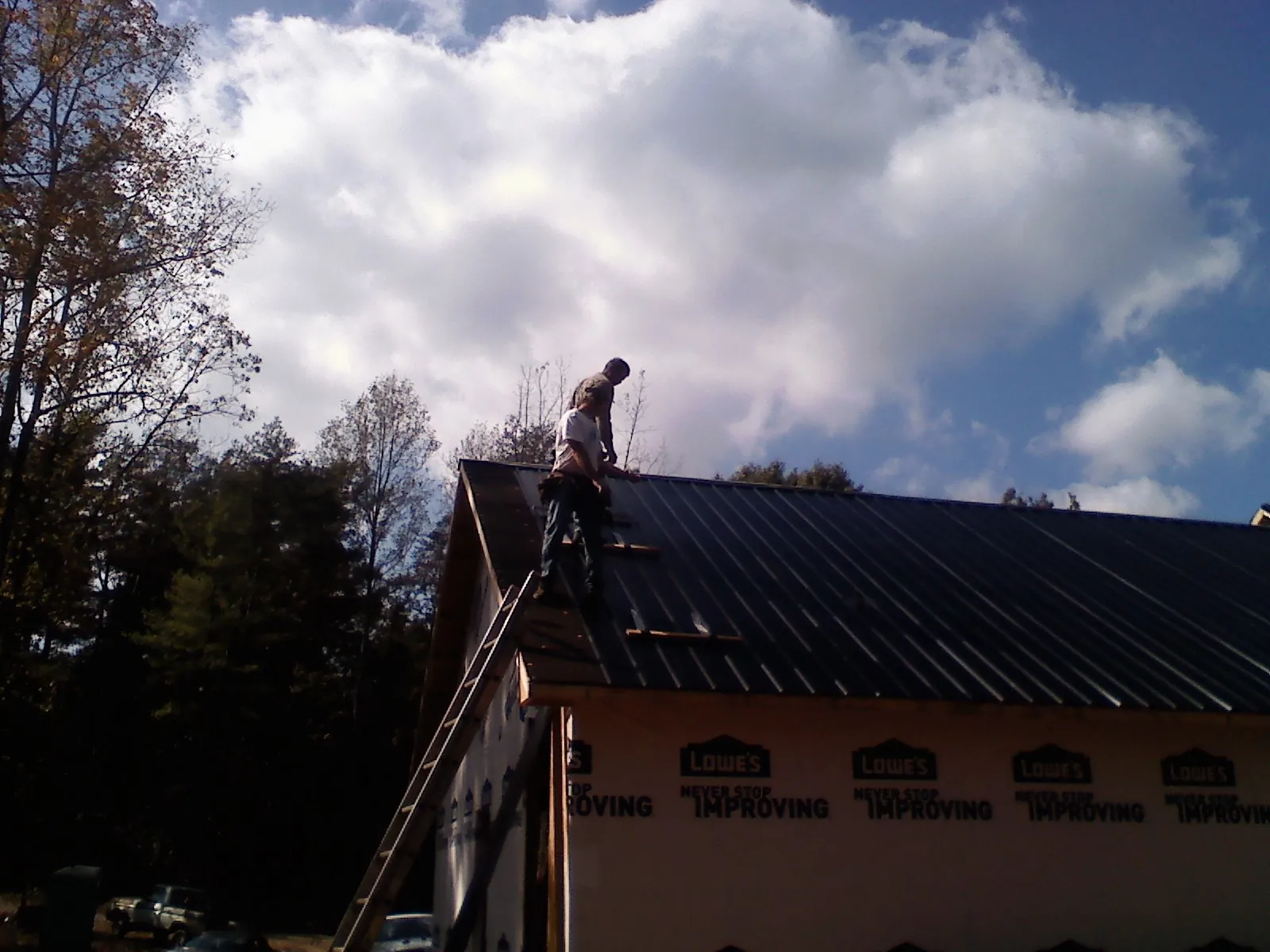 Roofer fastening dark metal panels high against a cloudy sky, from a Roof Inspection job in Medora