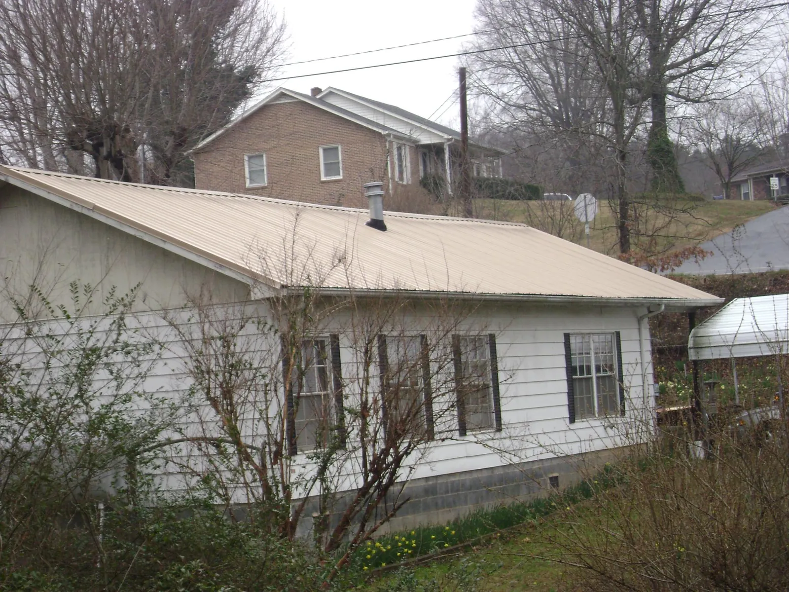 Tan metal roof on a white sided house set into a hillside — Commercial Roofing by Roofing Brothers in Medora