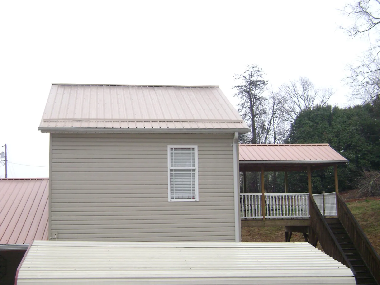 Tan metal roofs on a two story addition and attached porch, from a Roof Replacement job in Medora